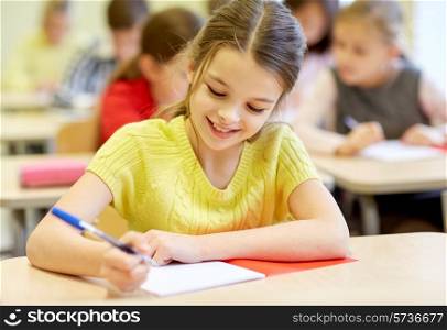 education, elementary school, learning and people concept - group of school kids with pens and notebooks writing test in classroom