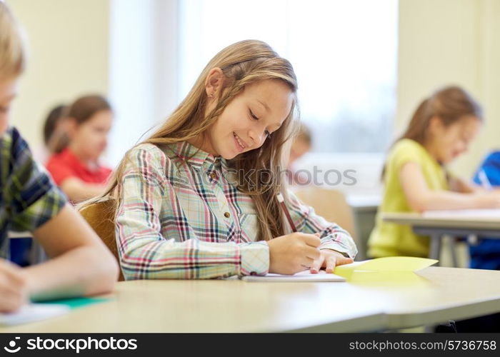 education, elementary school, learning and people concept - group of school kids with pens and notebooks writing test in classroom