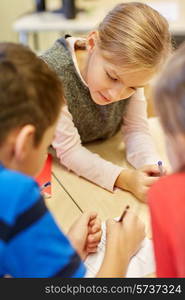 education, elementary school, learning and people concept - group of school kids with pens and papers writing in classroom