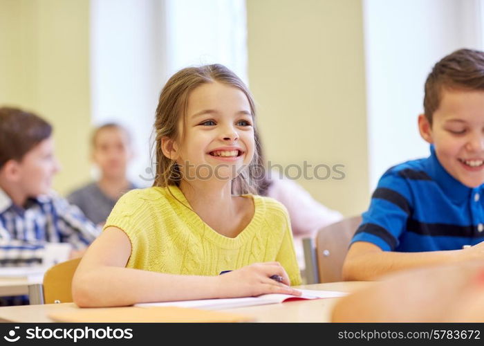 education, elementary school, learning and people concept - group of school kids with pens and notebooks writing test in classroom