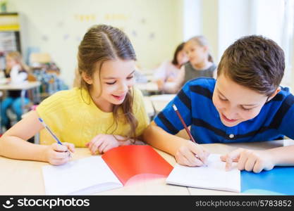 education, elementary school, learning and people concept - group of school kids with pens and notebooks writing test in classroom