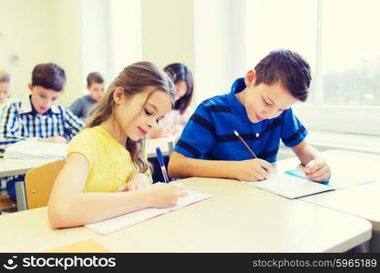 education, elementary school, learning and people concept - group of school kids with pens and notebooks writing test in classroom