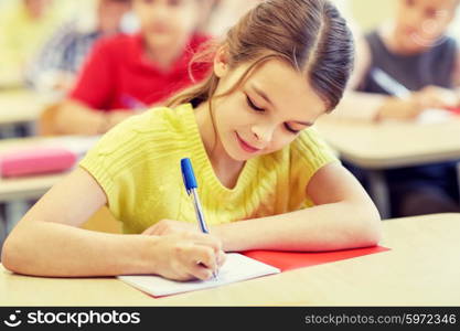 education, elementary school, learning and people concept - group of school kids with pens and notebooks writing test in classroom