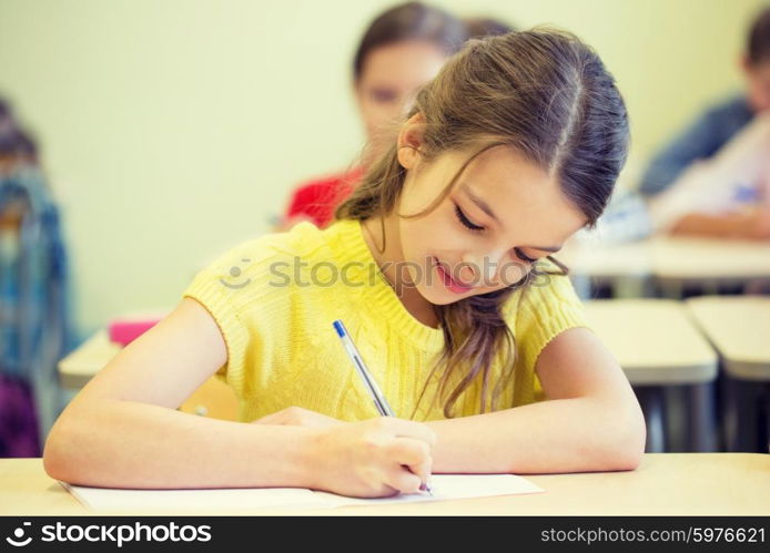 education, elementary school, learning and people concept - group of school kids with pens and notebooks writing test in classroom