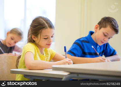 education, elementary school, learning and people concept - group of school kids with pens and notebooks writing test in classroom