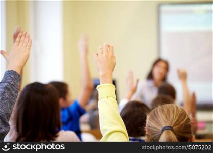education, elementary school, learning and people concept - group of students raising hands on lesson in classroom. group of school kids raising hands in classroom