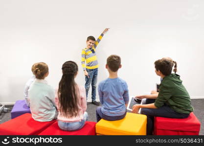 education, elementary school, learning and people concept - happy student boy showing something at white wall. happy student boy showing something at white wall