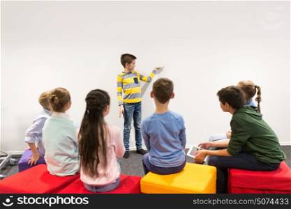 education, elementary school, learning and people concept - happy student boy showing something at white wall. happy student boy showing something at white wall
