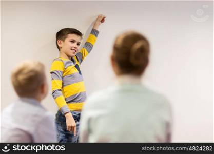 education, elementary school, learning and people concept - happy student boy showing to white wall