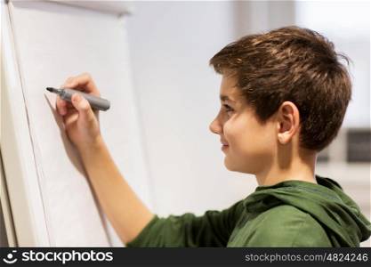 education, elementary school, learning and people concept - happy student boy with marker writing on flip board