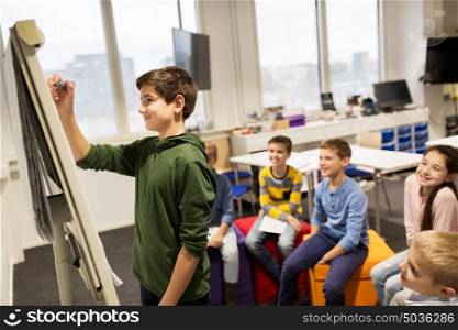 education, elementary school, learning and people concept - happy student boy with marker writing on flip board. student boy with marker writing on flip board