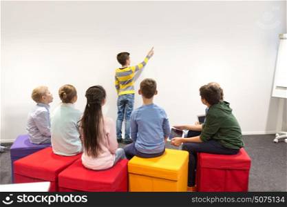 education, elementary school, learning and people concept - student boy with friends showing to white wall. student boy with friends showing to white wall