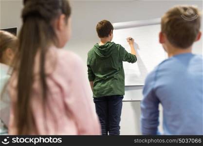 education, elementary school, learning and people concept - student boy with marker writing on flip board. student boy with marker writing on flip board