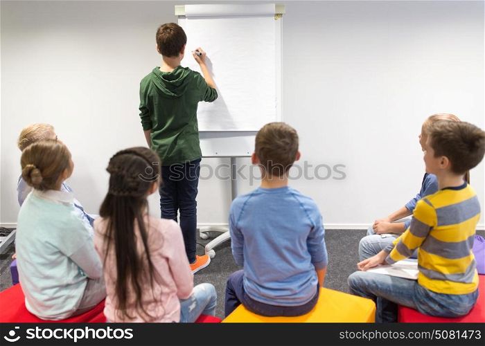 education, elementary school, learning and people concept - student boy with marker writing on flip board. student boy with marker writing on flip board