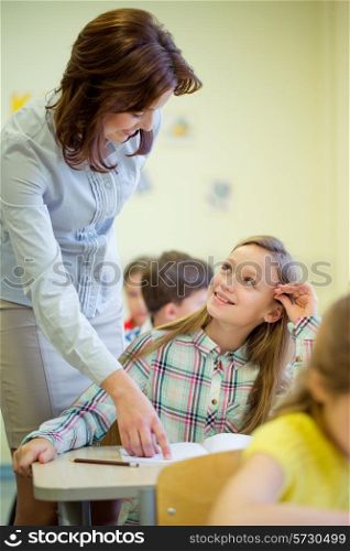 education, elementary school, learning and people concept - teacher helping school girl writing test in classroom