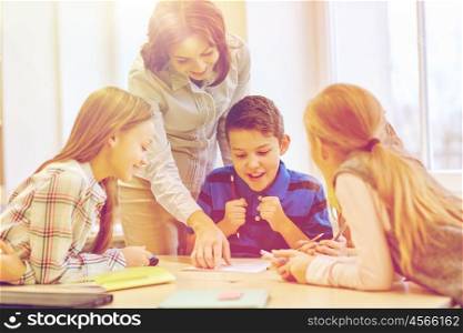 education, elementary school, learning and people concept - teacher helping school kids writing test in classroom