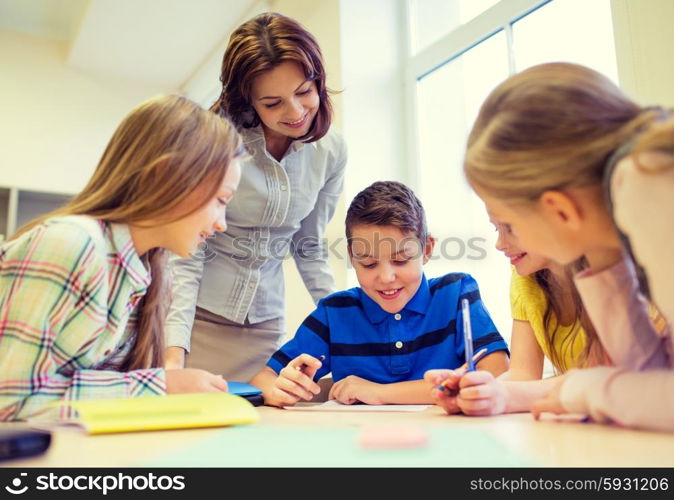 education, elementary school, learning and people concept - teacher helping school kids writing test in classroom