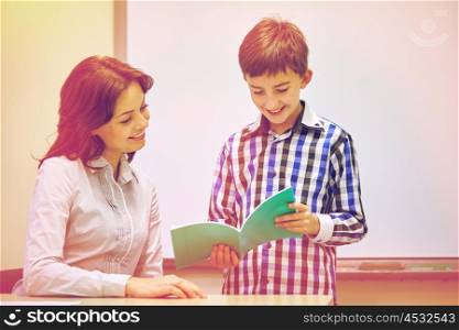 education, elementary school, learning, examination and people concept - school boy with notebook and teacher in classroom