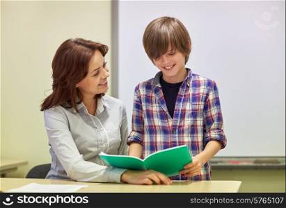 education, elementary school, learning, examination and people concept - school boy with notebook and teacher in classroom