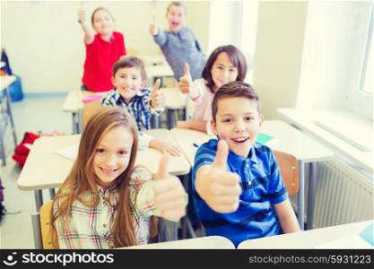 education, elementary school, learning, gesture and people concept - group of school kids sitting in classroom and showing thumbs up