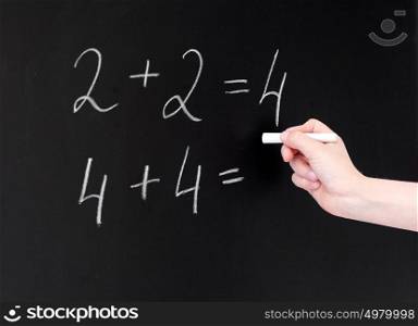 education, elementary school, learning, math and people concept - hand with chalk writing numbers on blackboard. hand with chalk writing numbers on blackboard