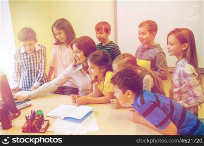 education, elementary school, learning, technology and people concept - group of school kids with teacher looking to computer monitor in classroom
