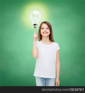 education, energy saving, advertising and people concept - smiling little girl in white blank t-shirt pointing finger up to light bulb over green chalk board background