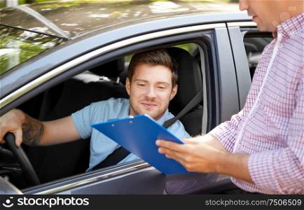 education, examination and people concept - driving school instructor with clipboard and male driver in car. car driving instructor with clipboard and driver