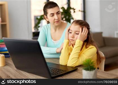 education, family and distant learning concept - mother and bored daughter with laptop computer doing homework together at home. mother and daughter with laptop doing homework
