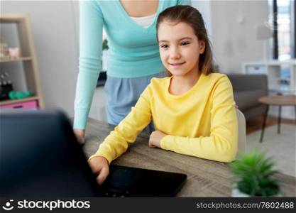 education, family and distant learning concept - mother and daughter with laptop computer doing homework together at home. mother and daughter with laptop doing homework
