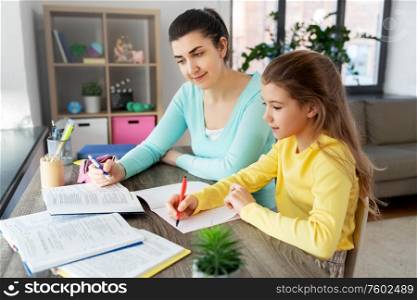 education, family and homework concept - happy mother and daughter with book writing to notebook at home. mother and daughter doing homework together