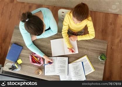 education, family and homework concept - mother and daughter with books writing to notebook at home. mother and daughter doing homework together
