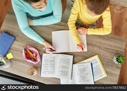 education, family and homework concept - mother and daughter with books writing to notebook at home. mother and daughter doing homework together