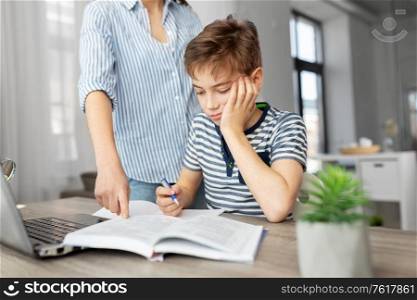 education, family and homework concept - mother and son with book writing to notebook at home. mother and son doing homework together