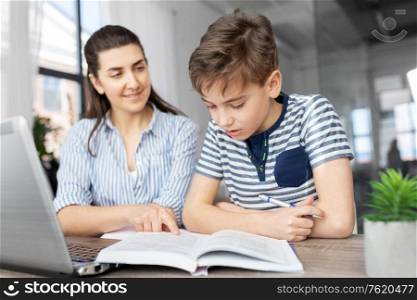 education, family and homework concept - smiling mother and son with book writing to notebook at home. mother and son doing homework together
