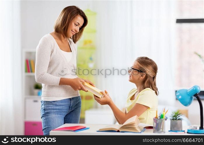 education, family and learning concept - happy mother giving daughter book at home. happy mother giving daughter book at home