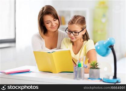 education, family and learning concept - mother and daughter doing homework together and reading book at home. mother and daughter doing homework together