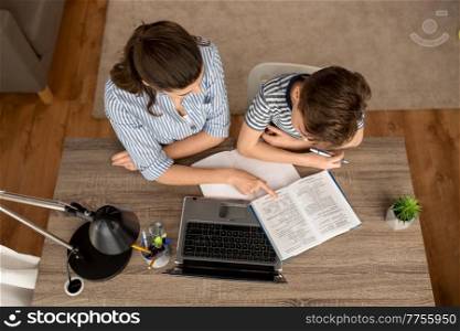 education, family and school concept - mother and son with book , notebook and laptop computer doing homework together at home. mother and son doing homework together