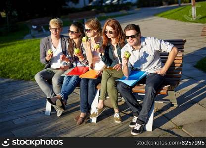 education, food, people and friendship concept - group of happy students eating green apples