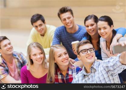 education, friendship, drinks, technology and people concept - group of smiling students with smartphone and paper coffee cup taking selfie at school
