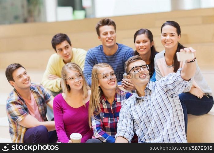 education, friendship, drinks, technology and people concept - group of smiling students with smartphone and paper coffee cup taking selfie at school