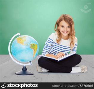 education, geography, childhood, people and school concept - little student girl studying with globe and book over green chalk board background