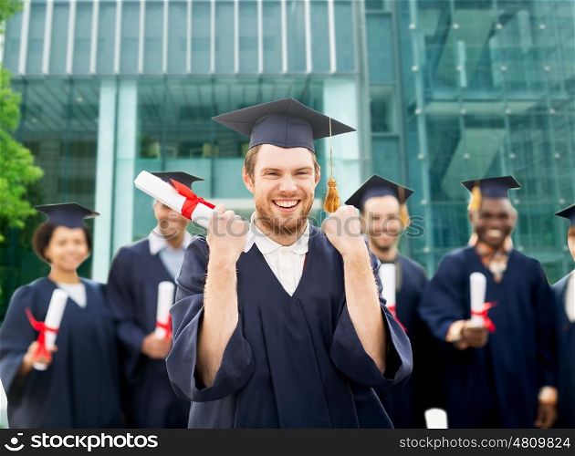 education, gesture and people concept - group of happy international students in mortar boards and bachelor gowns with diplomas celebrating successful graduation over university building background