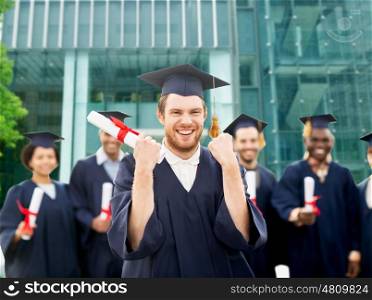 education, gesture and people concept - group of happy international students in mortar boards and bachelor gowns with diplomas celebrating successful graduation over university building background
