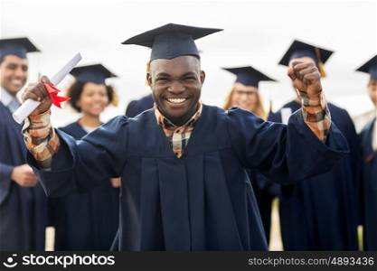 education, gesture and people concept - group of happy international students in mortar boards and bachelor gowns with diplomas celebrating successful graduation