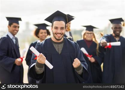 education, gesture and people concept - group of happy international students in mortar boards and bachelor gowns with diplomas celebrating successful graduation. happy student with diploma celebrating graduation