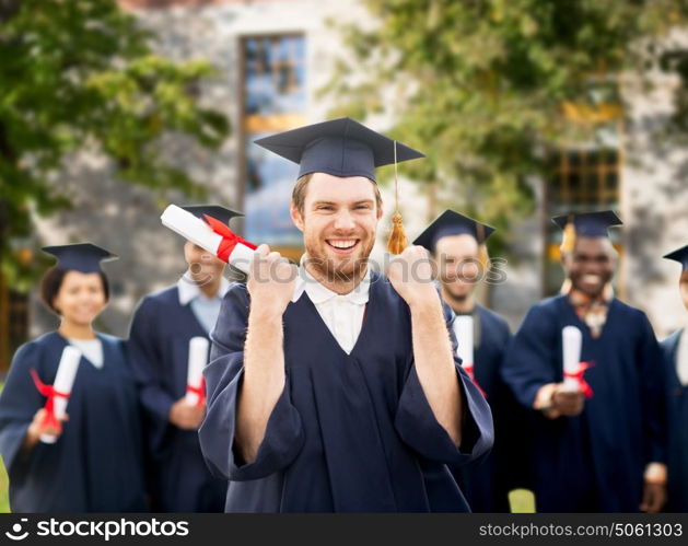 education, gesture and people concept - group of happy international students in mortar boards and bachelor gowns with diplomas celebrating successful graduation over campus building background. happy student with diploma celebrating graduation