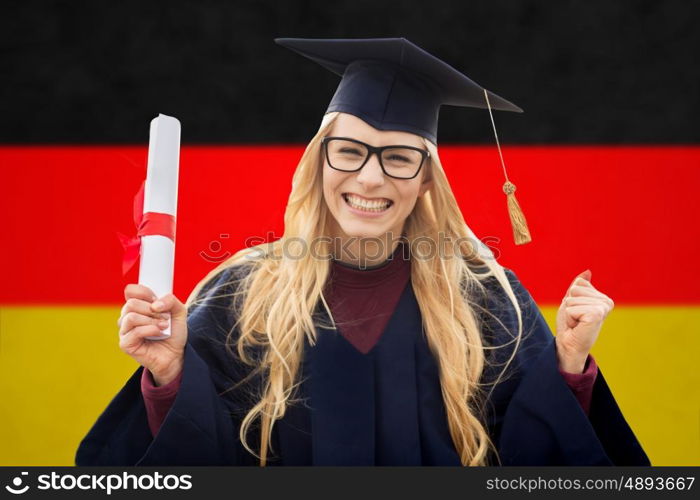 education, gesture and people concept - happy female student in mortar board and bachelor gown with diploma celebrating successful graduation over german flag background