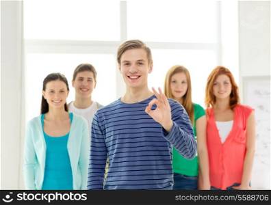 education, gesture and school concept - group of smiling students with teenage boy in front showing ok sign