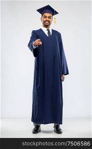 education, graduation and choice concept - happy smiling indian male graduate student in mortar board and bachelor gown pointing to you over grey background. indian graduate student pointing to you